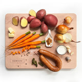 Aardappelen, wortels, uien en rookworst voor hutspot op een beukenhouten snijplank, van bovenaf