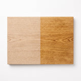 Een houten snijplank, verdeeld in twee helften. De linkerhelft is lichtgekleurd, de rechterhelft is donkerder en geolied.