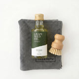 Fles druivenpitolie 40 ml met groen label, naast een grijze doek en een houten borsteltje.