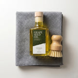 Een fles druivenpitolie van TheWootz staat op een grijze doek, naast een houten borsteltje.