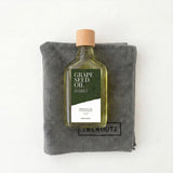 Fles druivenpitolie met houten dop op een grijs microvezeldoek. Label: GRAPE SEED OIL.