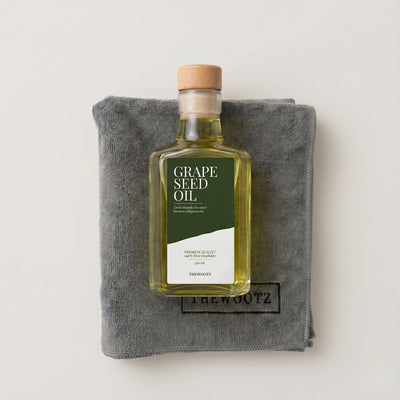 Fles druivenpitolie op een grijs microvezeldoek, met groen label 'GRAPE SEED OIL'.