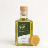 Fles druivenpitolie met een rond wax blok van bijenwas ernaast.